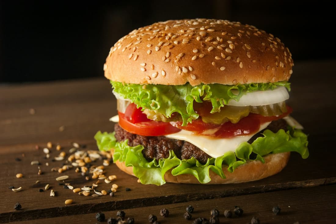 Burger im Sesambrötchen mit Käse, Tomate und Salat auf dunklem Holz