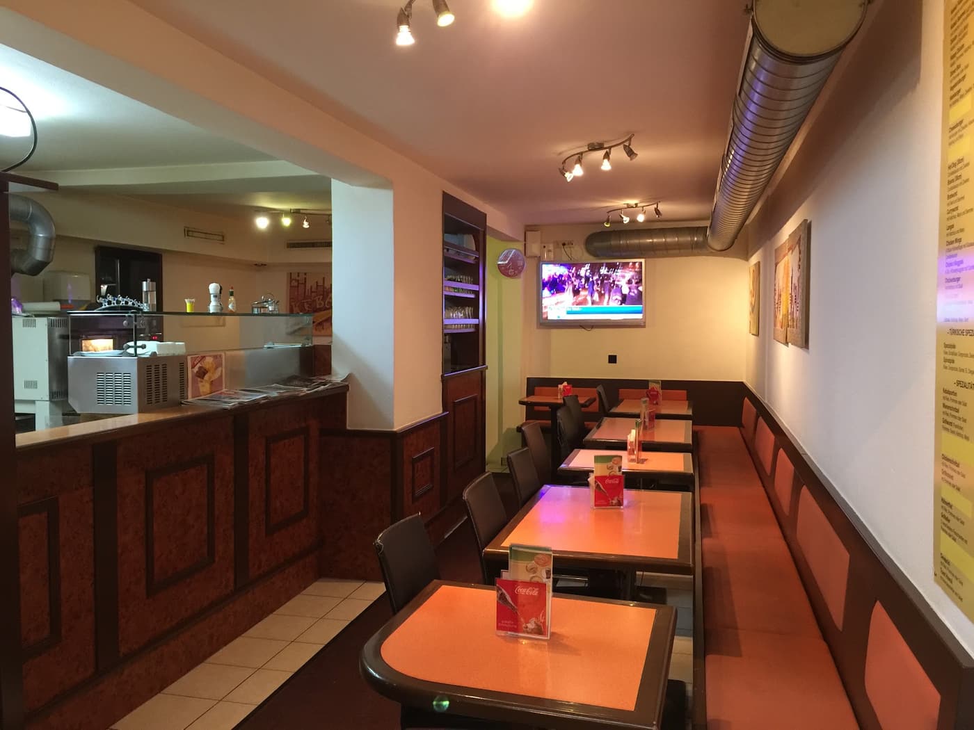 Gastraum von Happy Snack mit orangen Tischen, Sitzbank und Blick zur Theke