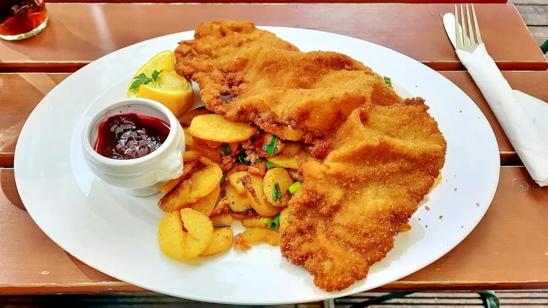 Paniertes Schnitzel mit Bratkartoffeln und Zitrone auf einem weißen Teller